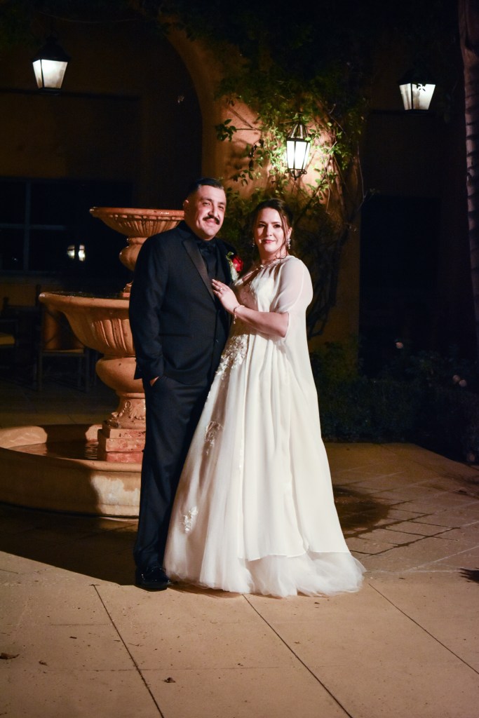 Formally dressed couple standing by a stone fountain at night