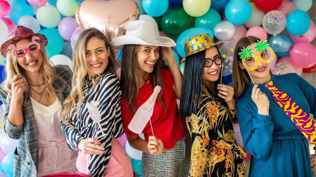 Five women posing with party props and champagne cutout in front of balloons