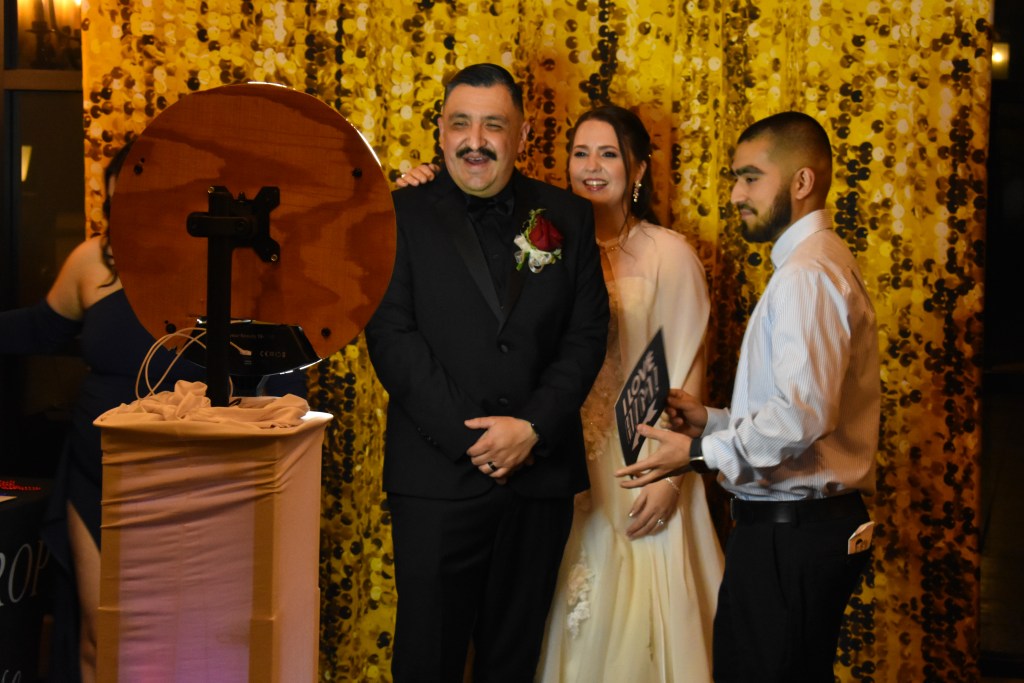 Wedding guests posing in front of golden sequin backdrop at photo booth