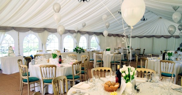 Elegant wedding marquee interior with round tables, white balloons, and floral centerpieces